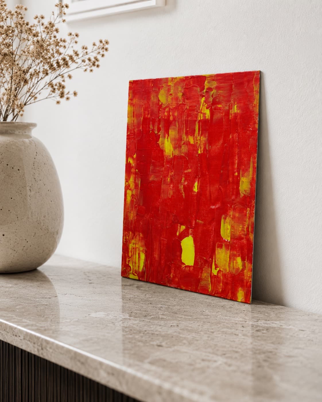 Amber Rain, a small red and yellow abstract painting by Julia Mindar with vertical drip, leaning against a wall
